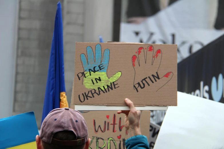 a person holding a sign at a protest, a photo, by Julia Pishtar, ukrainian flag on the left side, open palm, promo image, world peace