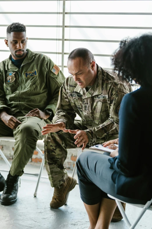 a group of people sitting around each other, military composure, diverse, talking, three