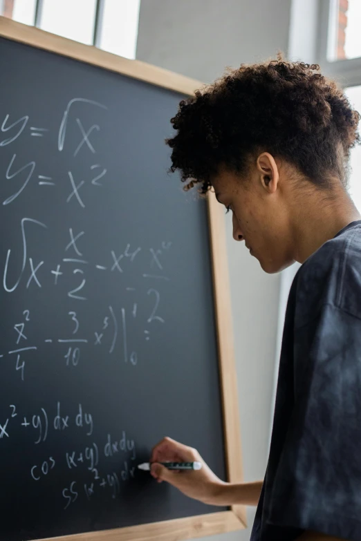 a woman standing in front of a blackboard writing on it, by Meredith Dillman, trending on unsplash, academic art, black teenage boy, balancing the equation, ignant, imaan hammam