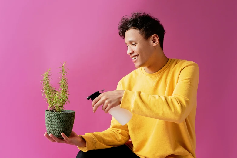 a man sitting on a stool holding a potted plant, by Julia Pishtar, pexels contest winner, pink and yellow, spraying liquid, male teenager, detailed product image