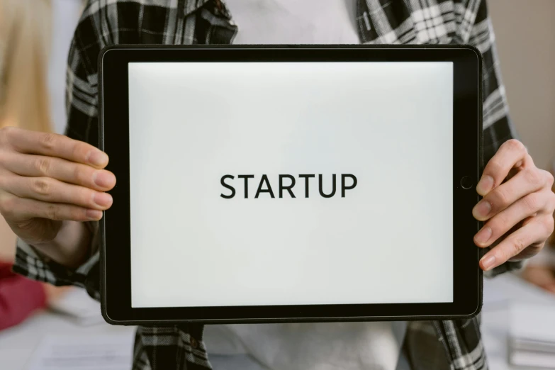 a person holding a tablet with the word startup on it, an album cover, square, background image, pc screen image