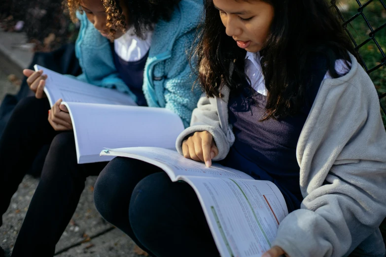 two girls sitting on a bench reading books, an album cover, by Alice Mason, pexels contest winner, school curriculum expert, closeup - view, looking at the ground, reading engineering book