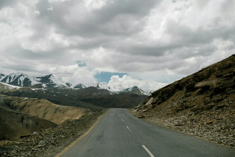 an empty road with mountains in the background, pexels contest winner, hurufiyya, breathtaking himalayan landscape, grey cloudy skies, subtitles, high elevation