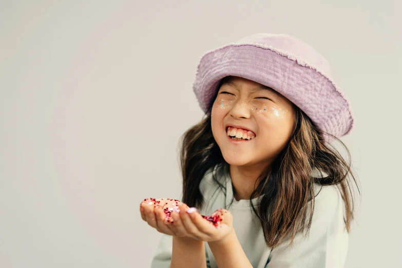 a little girl holding a donut with sprinkles on it, by Juliette Leong, trending on pexels, mingei, wearing a purple cap, photoshoot for skincare brand, mutahar laughing, hong june hyung