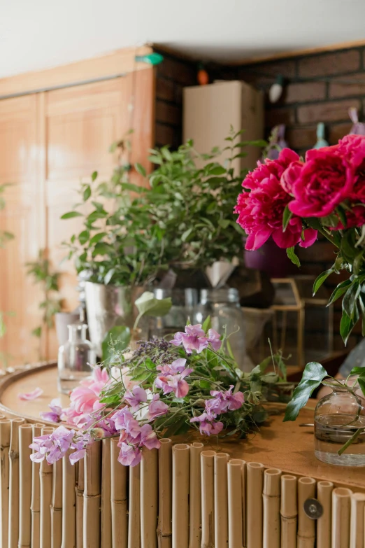 a bunch of flowers sitting on top of a wooden table, vases and bottles, flowering vines, indoor shot, pinks