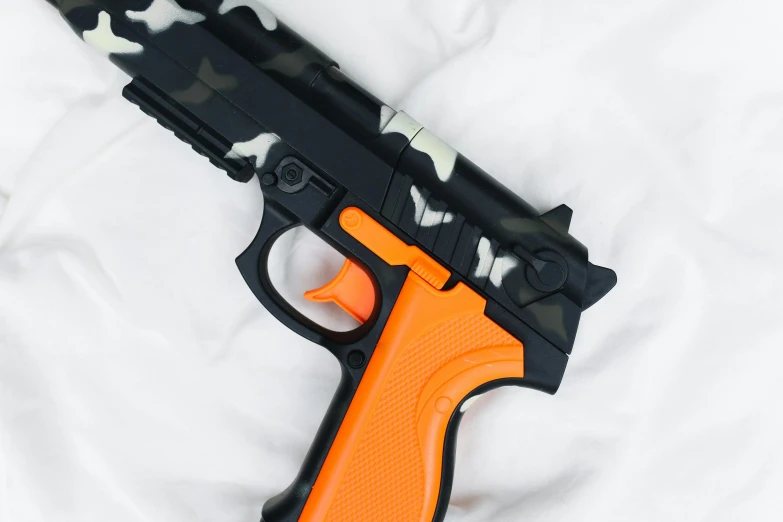 a toy gun laying on top of a bed, orange and black, jungle camo, close-up imagery, high quality product image”