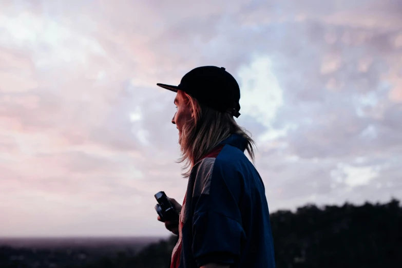 a man standing on top of a hill holding a cell phone, trending on pexels, young with long hair, lachlan bailey, profile portrait, end of the day