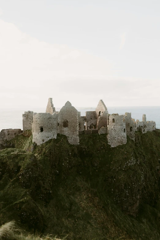 a castle sitting on top of a hill next to the ocean, castle ruins, cottages, a high angle shot, muted colors. ue 5