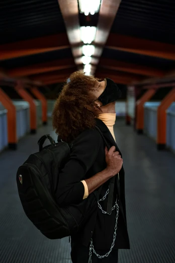 a person with a backpack standing in a hallway, by Fernando Gerassi, happening, the mask covers her entire face, subway station, hugging, profile image