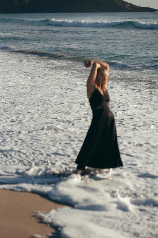 a woman standing on top of a beach next to the ocean, flowing black gown, crashing waves, zoomed in, profile image