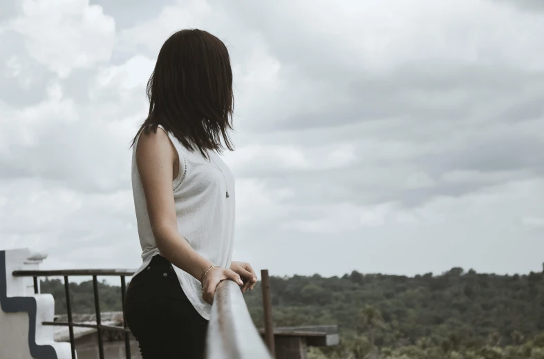 a woman standing on top of a wooden deck, pexels contest winner, clothed in white shirt, looking across the shoulder, background image, slight overcast weather