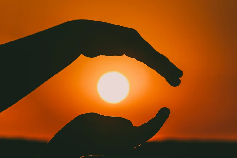 a person holding their hands in front of the sun, orange sky, high quality product image”, play of light, instagram post