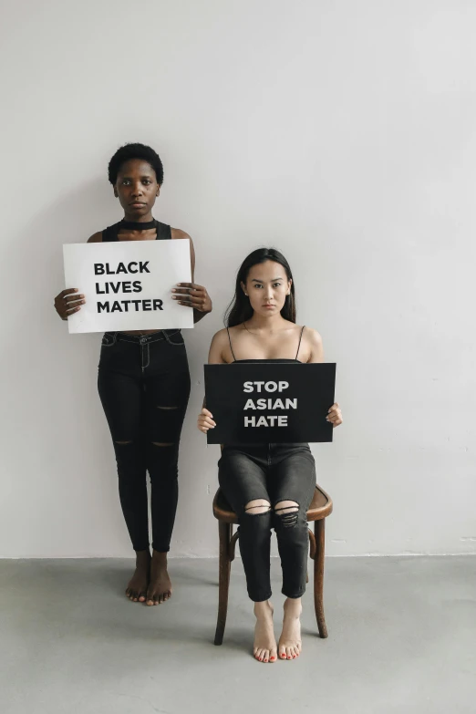 two women holding signs that read black lives matter and stop asian hate, trending on unsplash, sitting on a stool, plain background, instagram picture, darker skin