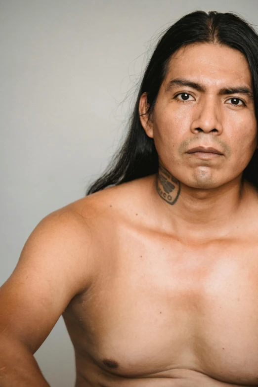 a man with a tattoo on his chest, inspired by Jorge Jacinto, trending on unsplash, hyperrealism, wearing a native american choker, with long hair and piercing eyes, non binary model, photographed for reuters
