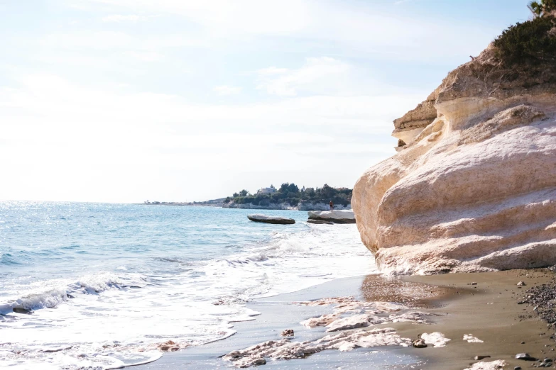 a man riding a surfboard on top of a sandy beach, unsplash, romanticism, cyprus, in the distance is a rocky hill, background image, geological strata