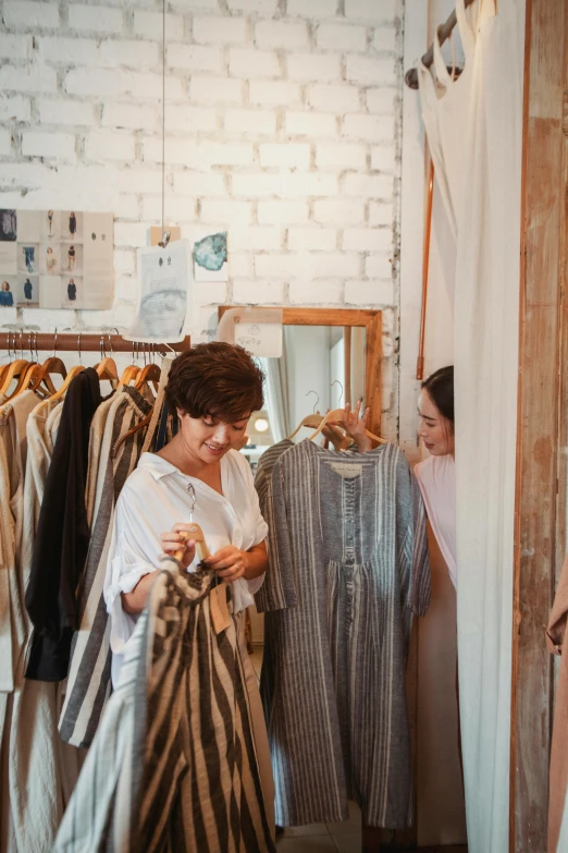 a woman standing in front of a rack of clothes, woman holding another woman, wearing a linen shirt, australian, a cozy