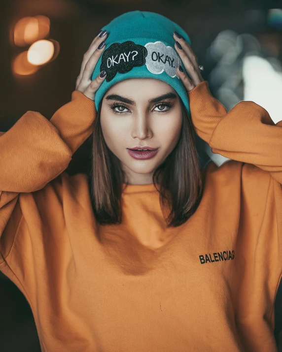 a woman wearing an orange sweatshirt and a green hat, inspired by Elsa Bleda, trending on pexels, wearing teal beanie, okay one fear, non binary model, product introduction photo