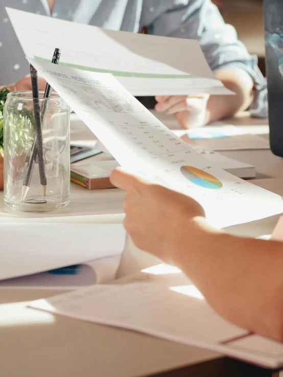 a group of people sitting around a table with papers, up close picture, thumbnail, high quality image