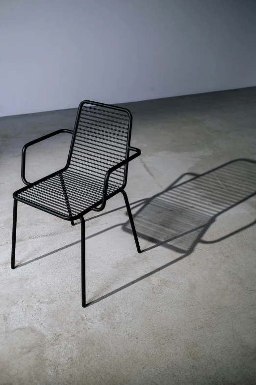 a black chair sitting on top of a cement floor, by Jan Jahn, unsplash, op art, made of wire, long shadow, bench, square