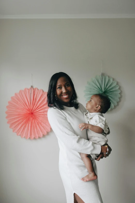 a woman holding a baby in her arms, an album cover, by Dulah Marie Evans, pexels contest winner, hurufiyya, portrait photo of a backdrop, looking confident, celebration, indoor picture