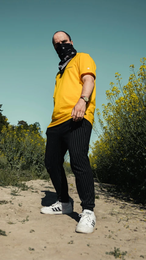 a man wearing a mask standing on a dirt road, an album cover, unsplash, black. yellow, wearing polo shirt, alluring plus sized model, cinematic outfit photo
