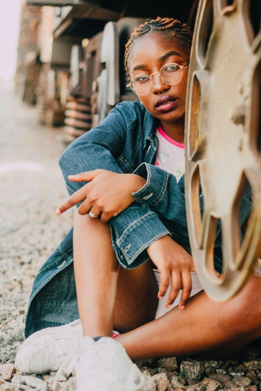 a woman sitting on the ground next to a train, a portrait, trending on pexels, willow smith young, wearing round glasses, denim, full frame image