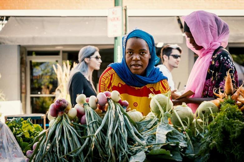 a woman standing in front of a table full of vegetables, by Meredith Dillman, hurufiyya, street market, somali attire, thumbnail, afropunk