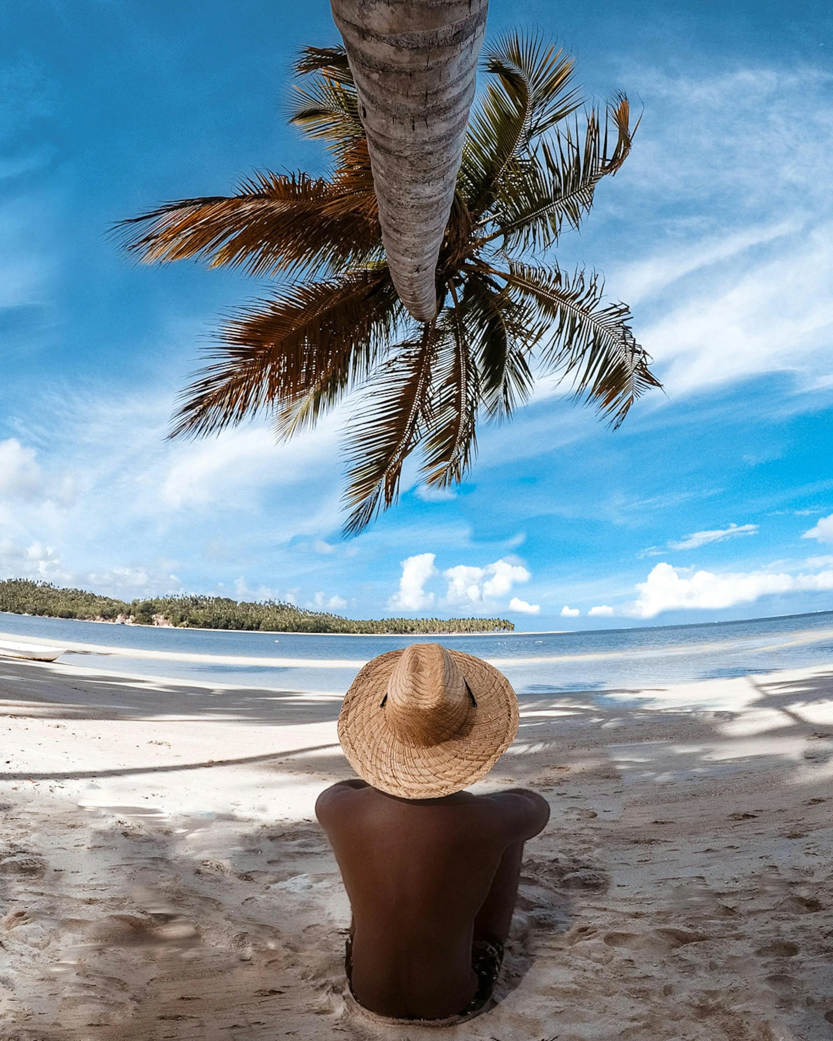 a man sitting under a palm tree on a beach, photo of the middle of the ocean, thumbnail, woman with hat, trending photo