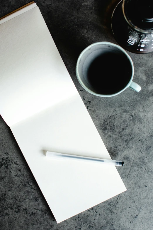 a notepad sitting on top of a table next to a cup of coffee, by Robbie Trevino, unsplash, process art, grey, promo image, no - text no - logo, black