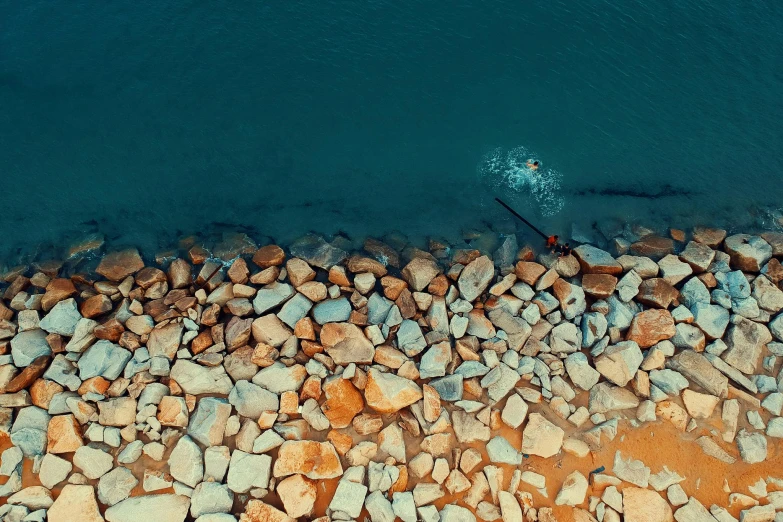 a person riding a surfboard on top of a rocky beach, inspired by Elsa Bleda, unsplash contest winner, minimalism, birdseye view, teal orange color palette 8k, alessio albi, small fish swimming around