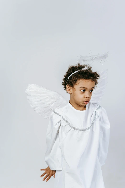 a little girl dressed up as an angel, an album cover, pexels contest winner, plain background, looking to the side off camera, high resolution product photo, wearing festive clothing