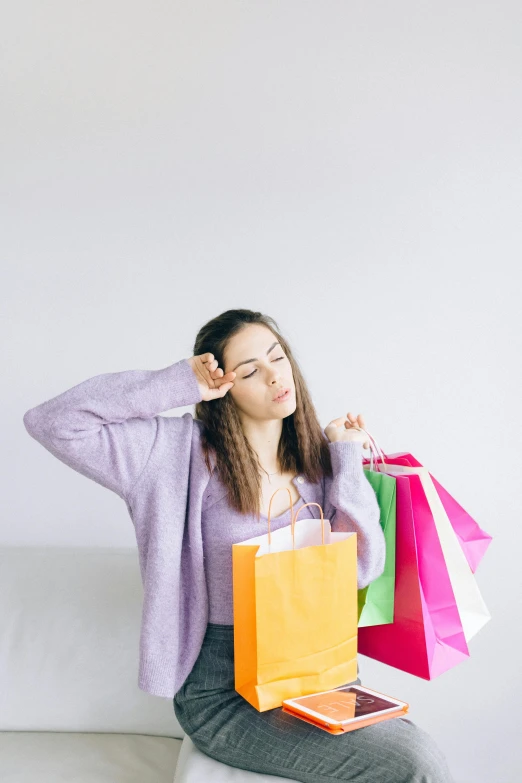 a woman sitting on a couch holding shopping bags, a colorized photo, pexels, renaissance, woman very tired, stands in center with open arms, on grey background, pink clothes