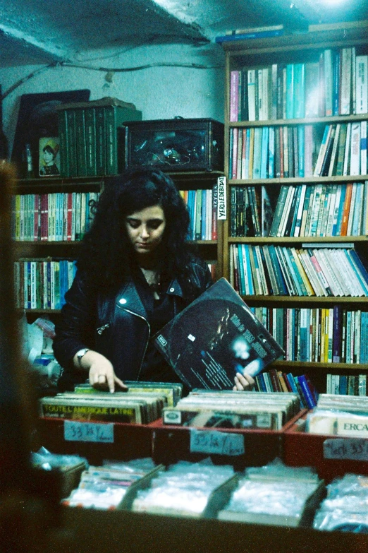 a woman standing in front of a book shelf filled with books, an album cover, inspired by Elsa Bleda, private press, retro punk, woman with black hair, 3 5 mm color, performing