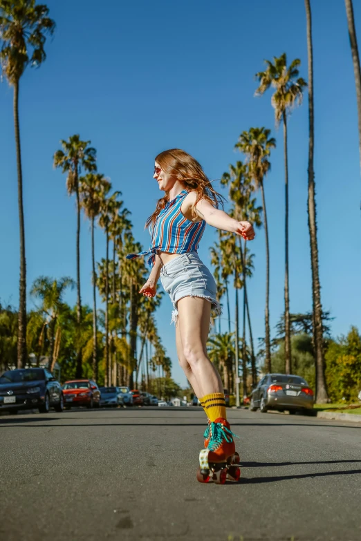 a woman riding a skateboard down a street next to palm trees, unsplash contest winner, renaissance, colorful outfit, california;, profile image, rollerskaters