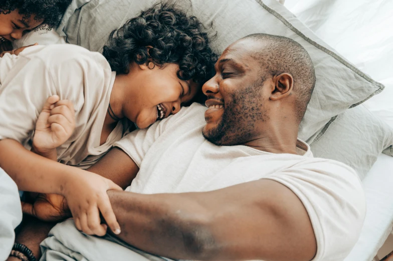 a man and two children laying on a bed, pexels contest winner, smiling at each other, african american, dad bod, profile image