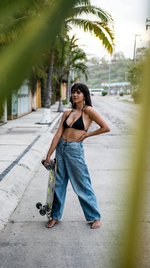 a woman standing on the side of a road holding a skateboard, by Olivia Peguero, halter-top, sports photo, isabela moner, resort