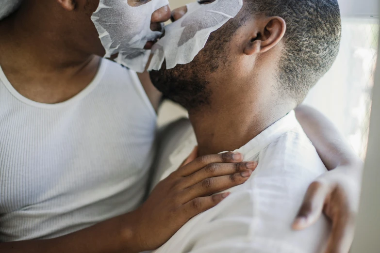 a man putting a mask on a woman's face, by Ellen Gallagher, trending on pexels, lesbian embrace, yoruba body paint, wearing translucent sheet, two men hugging