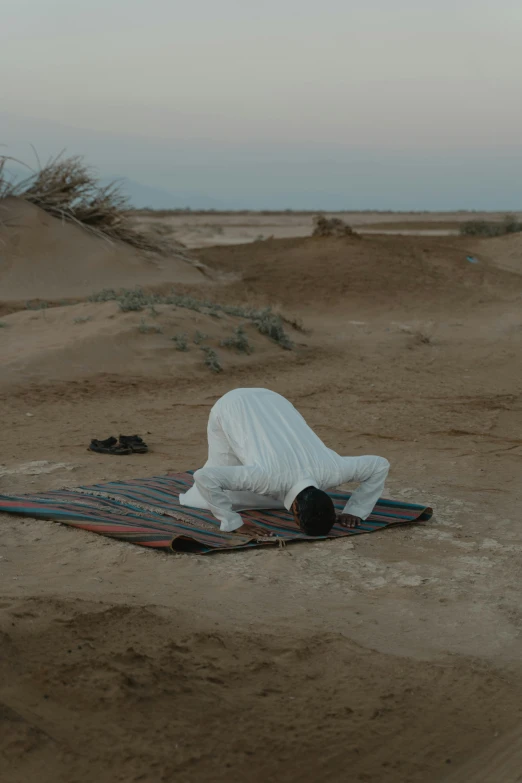 a person laying on a blanket in the desert, bent over posture, sufism, ignant, recreation