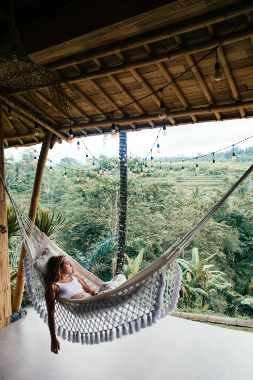 a woman sitting in a hammock on a porch, trending on unsplash, bali, lush countryside, panoramic centered view of girl, treehouse