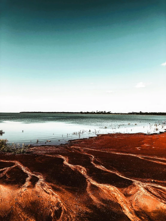 a large body of water sitting on top of a sandy beach, an album cover, red lake, australian outback, high-quality photo, photo on iphone