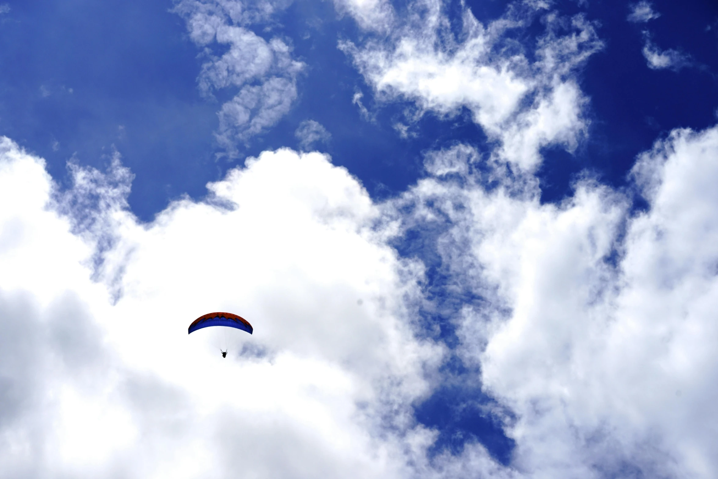 a paraglider flying through a cloudy blue sky, by Niko Henrichon, hurufiyya, fan favorite, mixed art, mundane, conde nast traveler photo