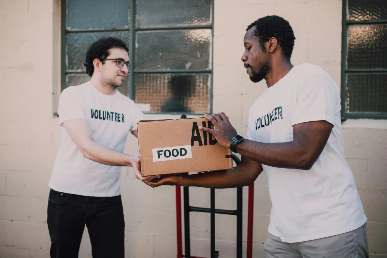 two men standing next to each other holding a box, by Julia Pishtar, pexels contest winner, hunger, avatar image, diverse, serving body