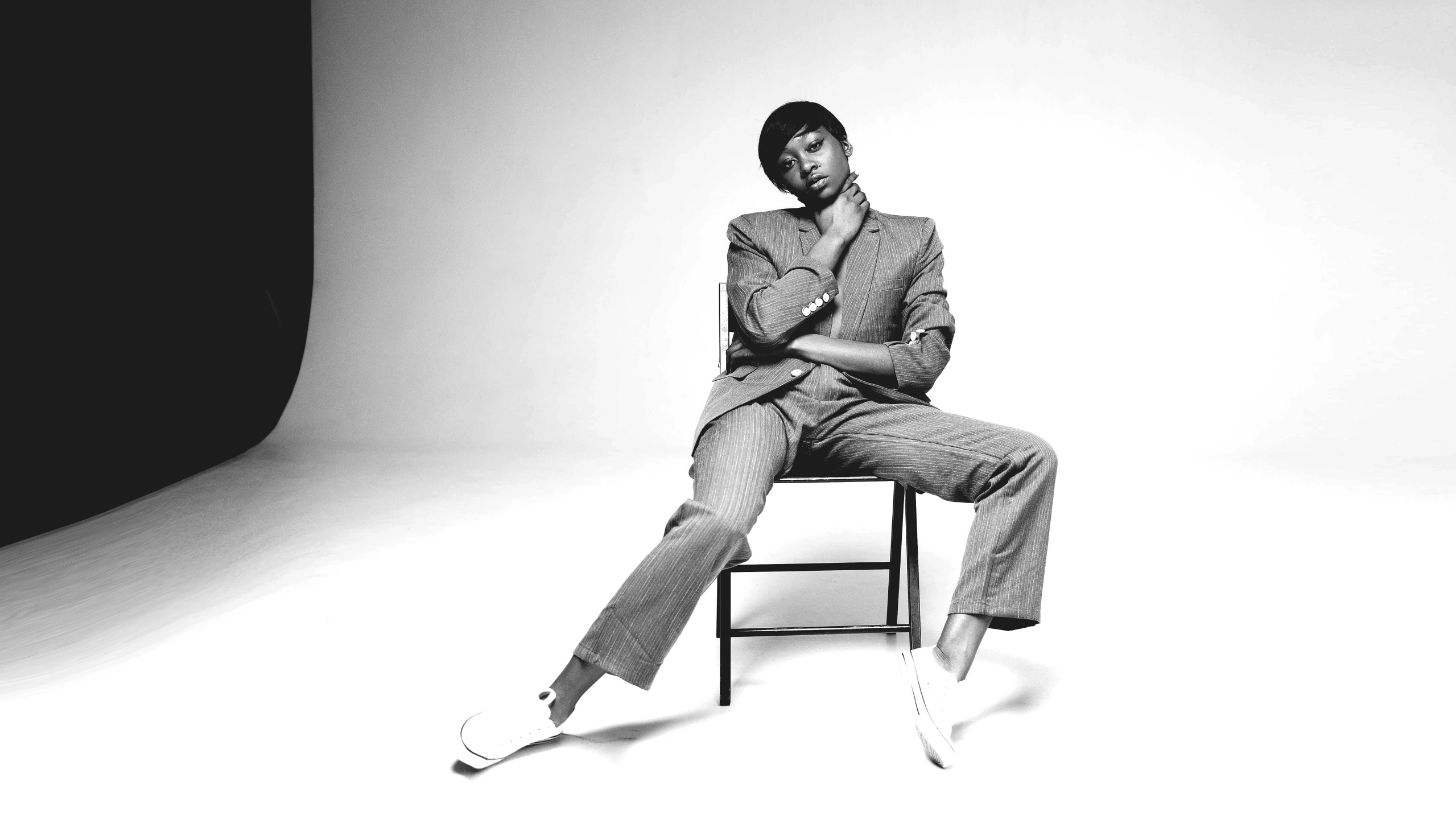 a black and white photo of a man sitting on a chair, by Dean Ellis, pexels, harlem renaissance, naomi campbell, wearing fashion suit, hyung tae, pastel'