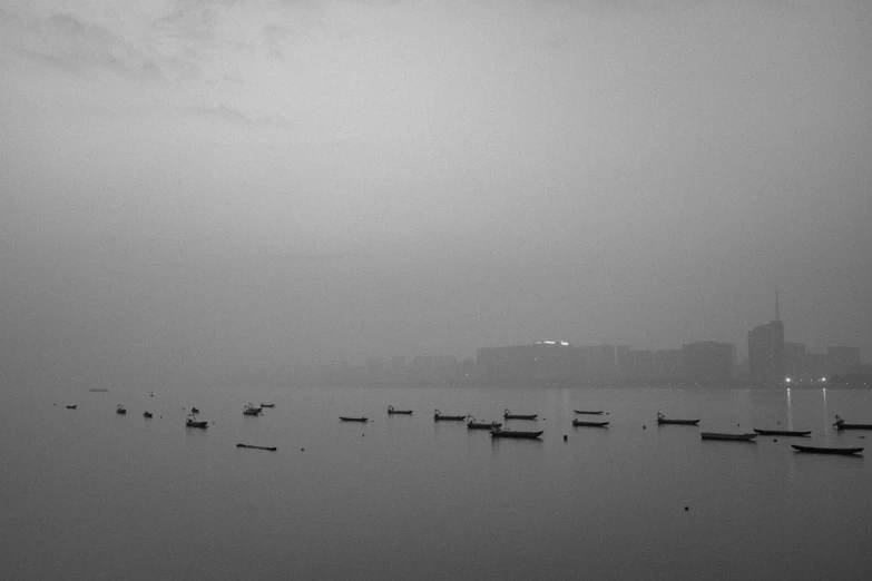 a group of boats floating on top of a body of water, a black and white photo, by Sudip Roy, minimalism, city fog, gloomy weather. high quality, :: morning, zezhou chen