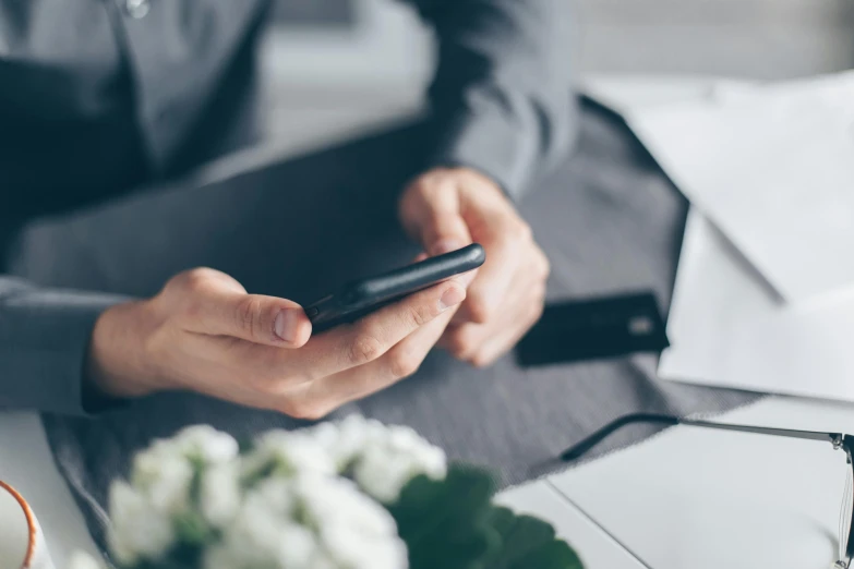 a close up of a person holding a cell phone, trending on pexels, sitting at desk at keyboard, flowers around, slick elegant design, avatar image