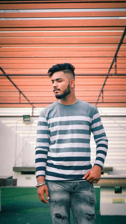 a man standing with his hands in his pockets, inspired by Ismail Acar, pexels contest winner, hurufiyya, striped sweater, gray color, zayn malik, indian