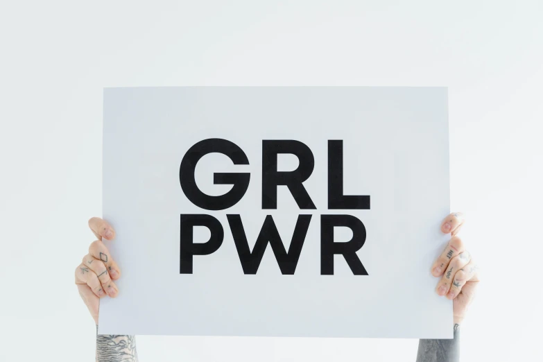 a person holding a sign that says grl pwr, an album cover, trending on pexels, feminist art, on grey background, high resolution print :1 cmyk :1, power girl, closeup photograph