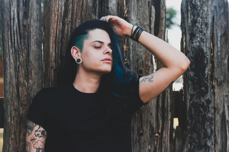 a person standing in front of a wooden fence, inspired by Elsa Bleda, pexels contest winner, antipodeans, tribal piercing and tatoos, jet black hair, androgynous person, next to a tree