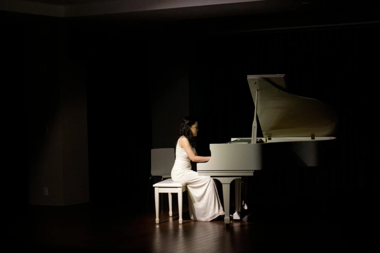 a woman sitting at a piano in a dark room, inspired by Fei Danxu, in a long white dress, live performance, plain background, taken with sony alpha 9