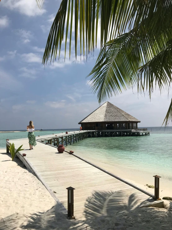 a woman standing on a pier next to a body of water, maldives in background, slide show, multiple stories, beach pic